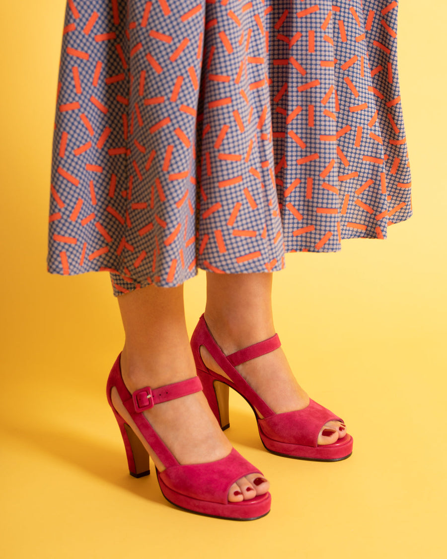 A person wearing Begum Paris Saint- Raphaël heeled sandals bright pink pants and red-and-purple high-heeled sandals poses against a light purple background.